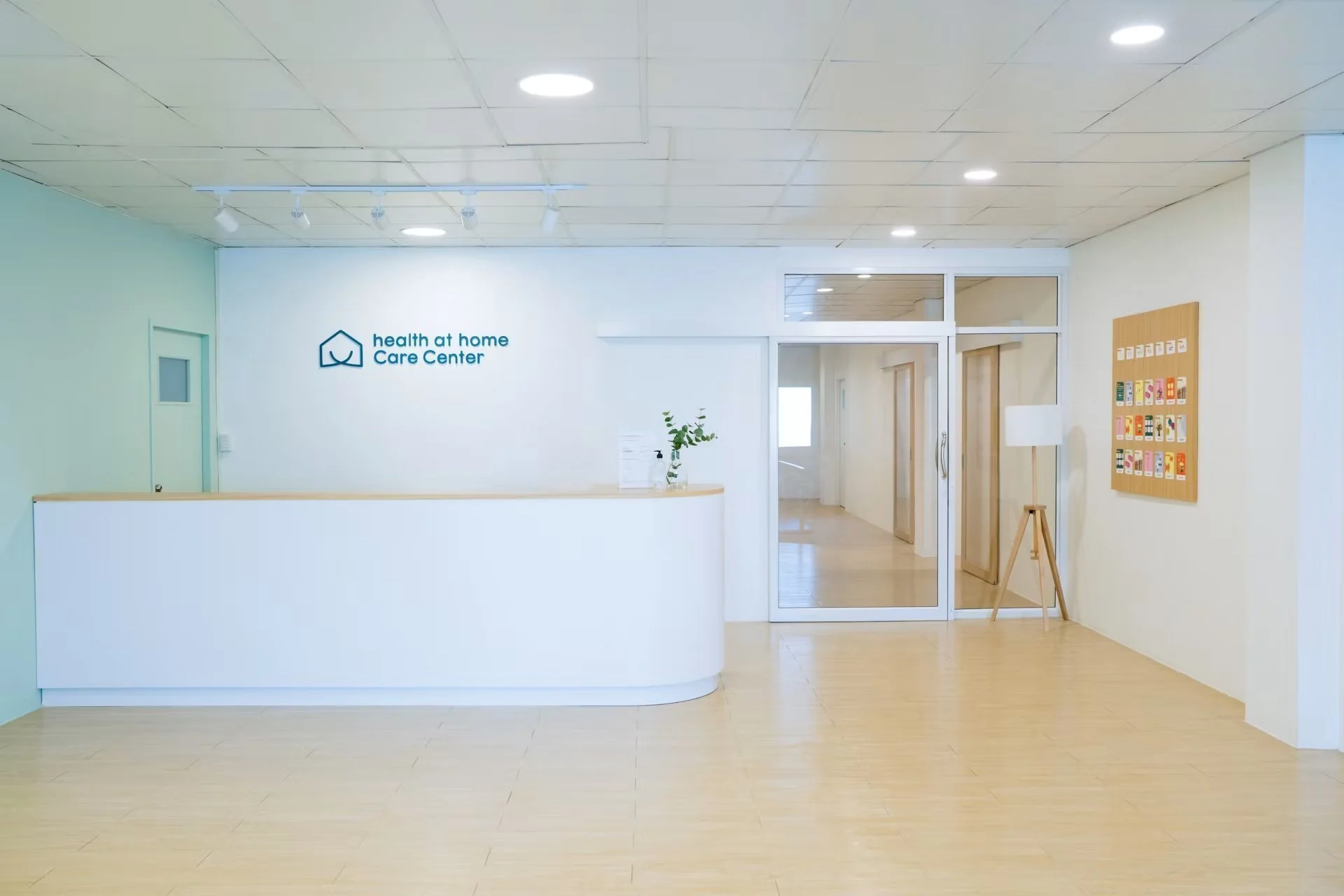 Recepção moderna com balcão branco, logo 'health at home Care Center', corredor e painel decorativo