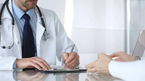 Médico de jaleco e estetoscópio escrevendo em prancheta durante consulta com paciente