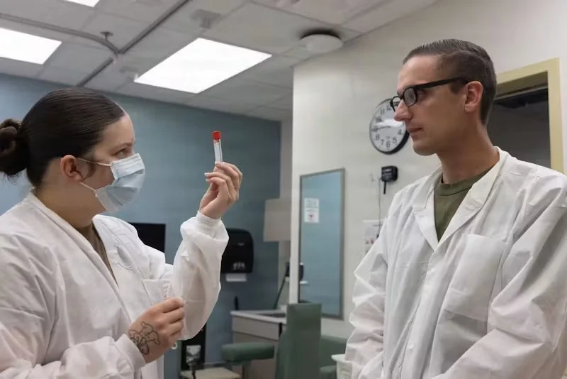 Duas pessoas em jalecos brancos em um laboratório. Uma segura um tubo de ensaio, a outra observa