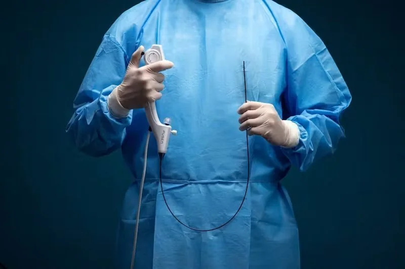 Profissional de saúde em avental cirúrgico azul e luvas, segurando um dispositivo médico PUSEN e um tubo flexível