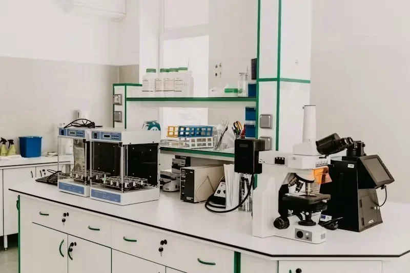 Laboratório moderno com bancadas brancas, equipamentos científicos, microscópios e prateleiras com frascos