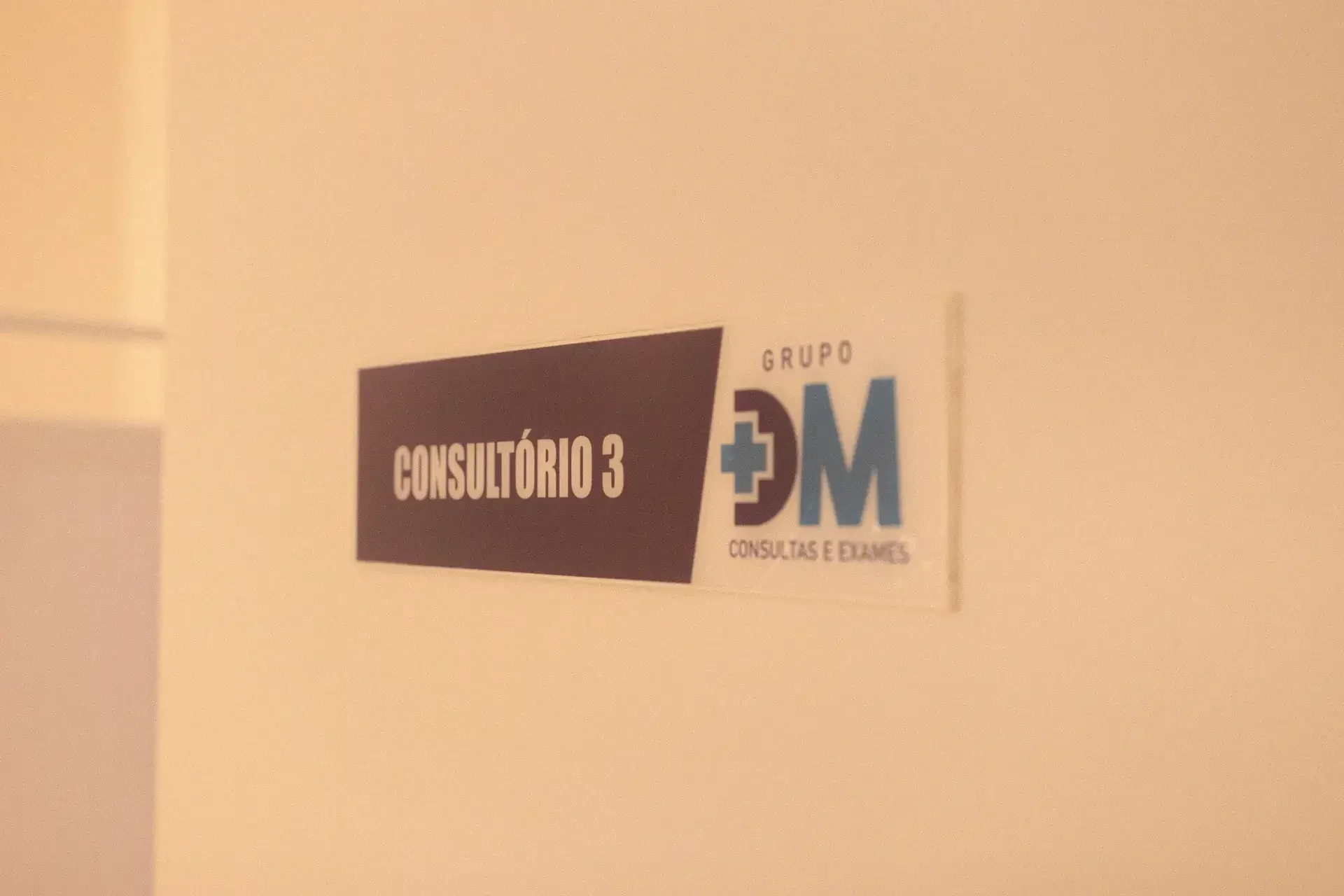 Placa de consultório com 'CONSULTÓRIO 3' e logo 'GRUPO DM CONSULTAS E EXAMES